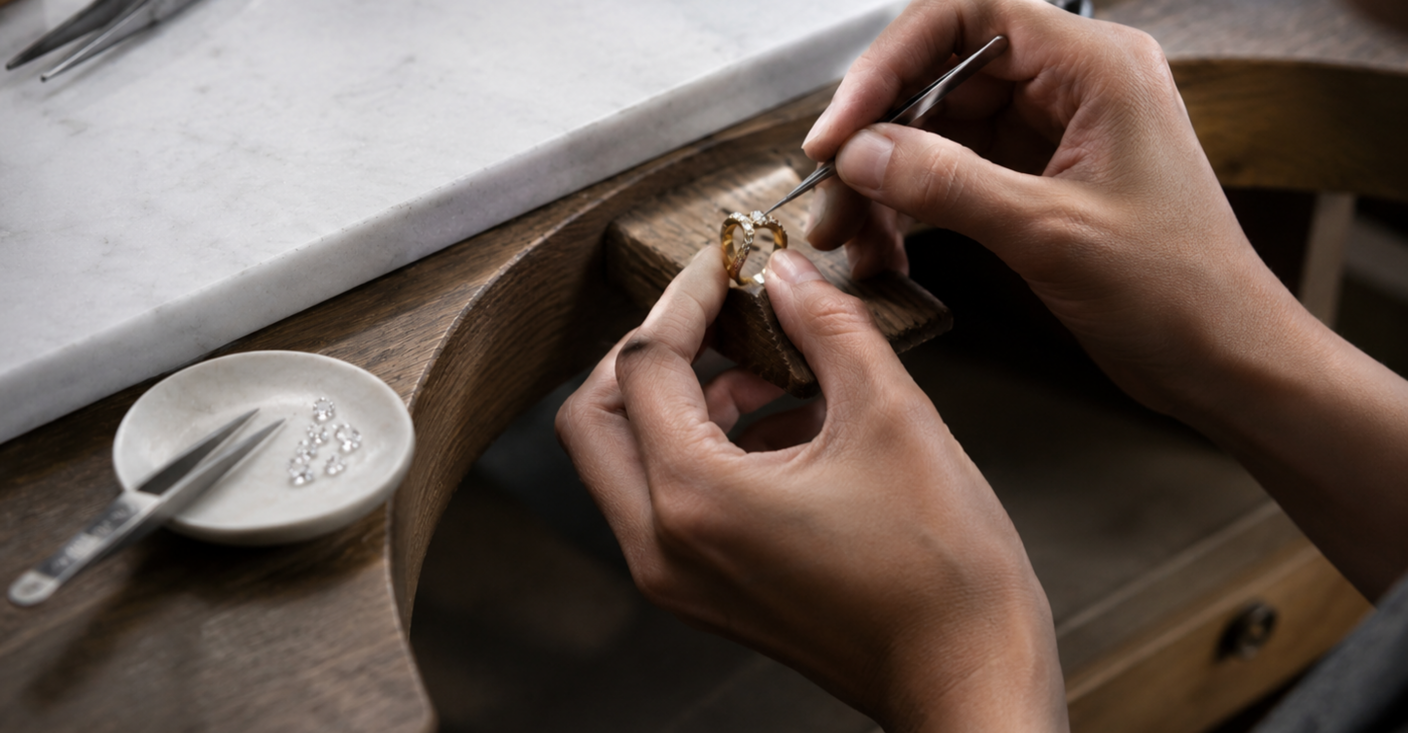Close-up of hands working on a piece of jewelry with tools and materials on a table.