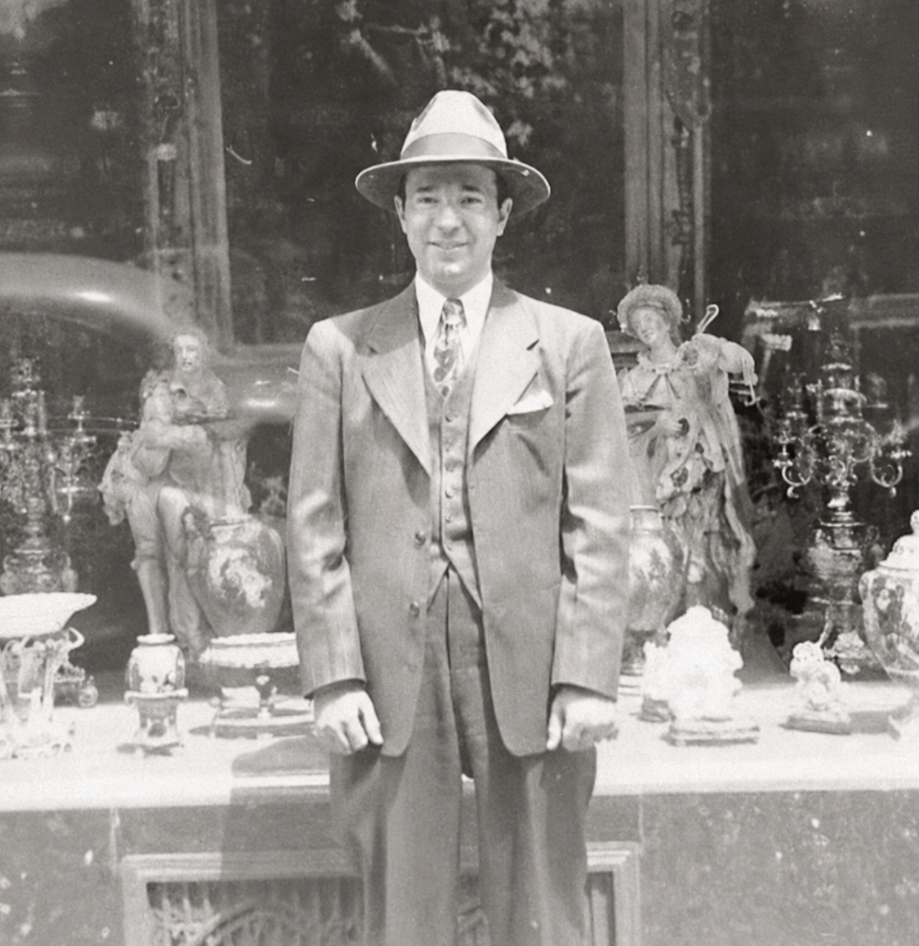 Albert DeSerio in a suit and hat standing in front of decorative items