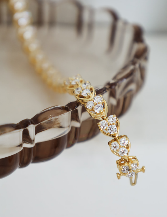 A gold-toned bracelet with a dangling chain of heart-shaped clear gemstone clusters, photographed close up against a soft light background.