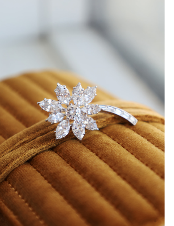 A floral brooch with clear marquise and round-cut stones, displayed on a brown velvet jewelry box.