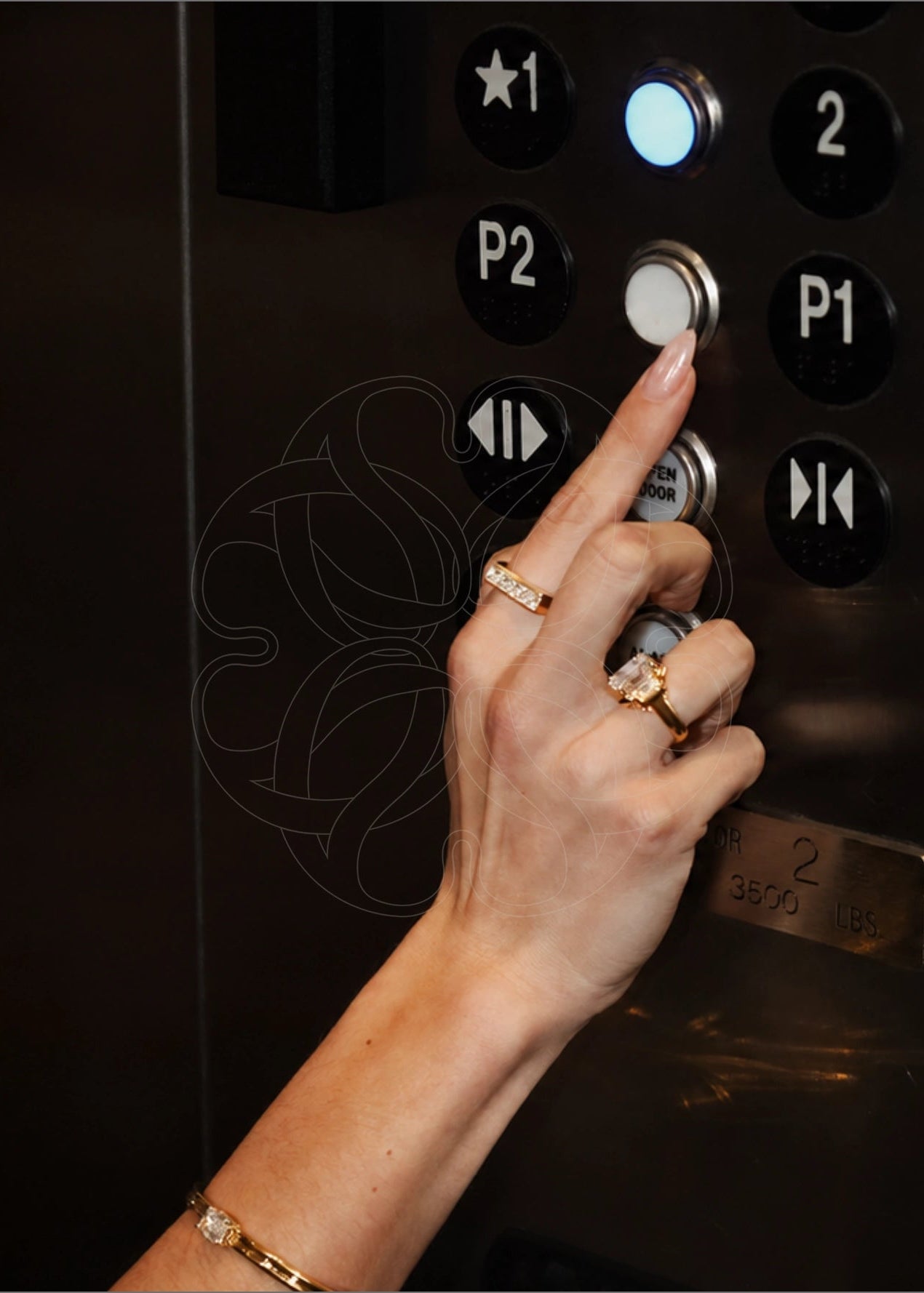 A close-up of a woman's hand pressing a an elevator button wearing fine jewelry rings