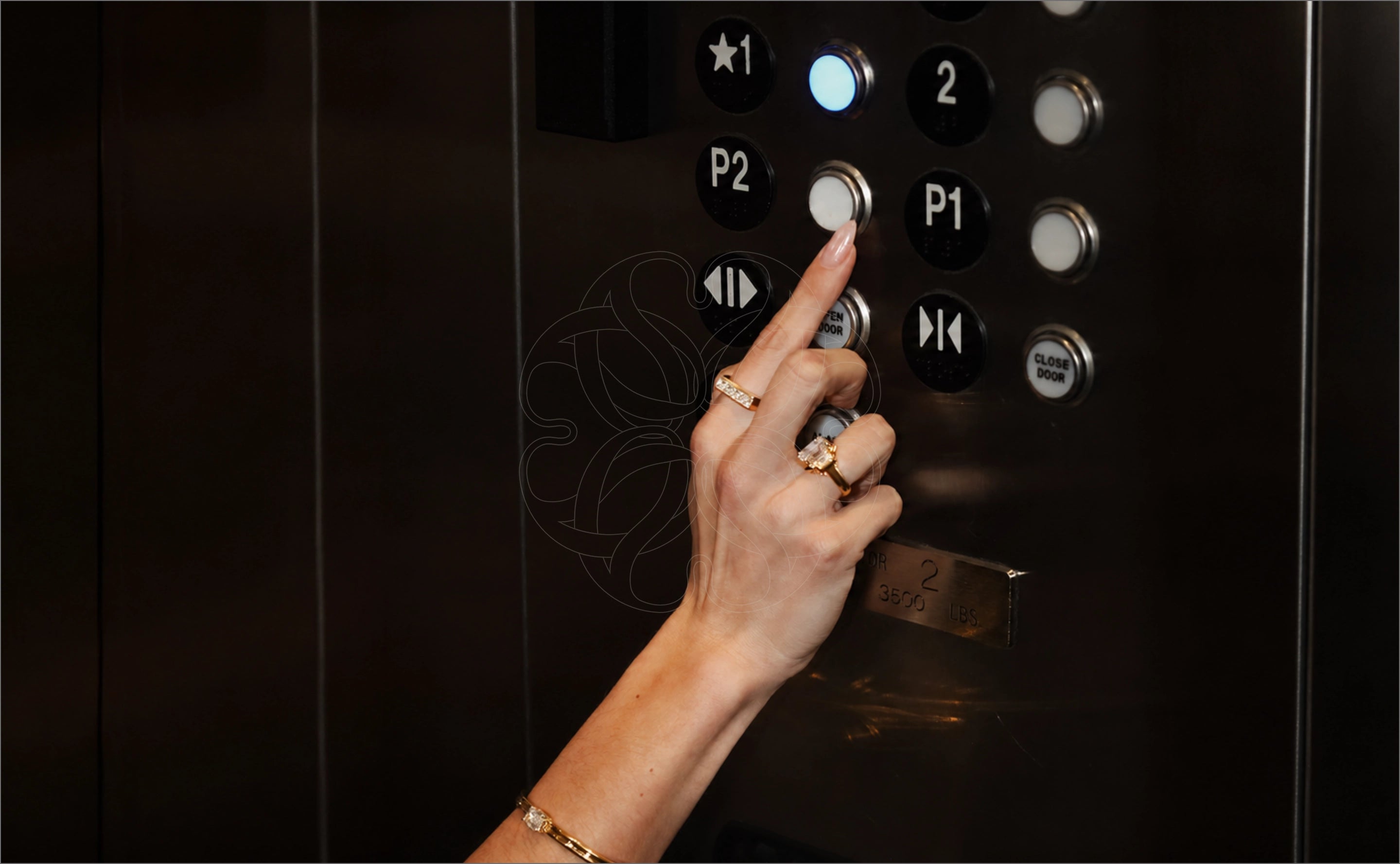 A close-up of a woman's hand pressing a an elevator button wearing fine jewelry rings
