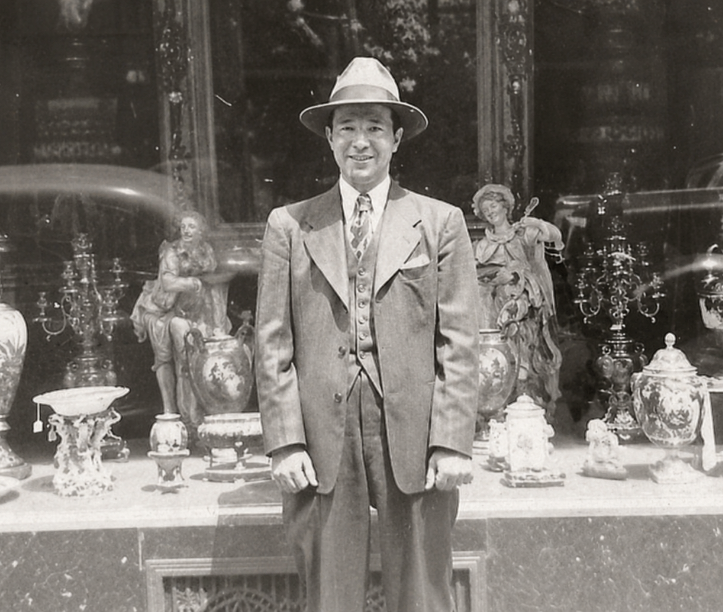 Albert DeSerio in a suit and hat standing in front of a display case with decorative items.